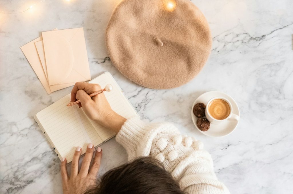Personne écrivant dans un carnet à côté d'une tasse de café, pour suivre ses repas et ses symptômes digestifs