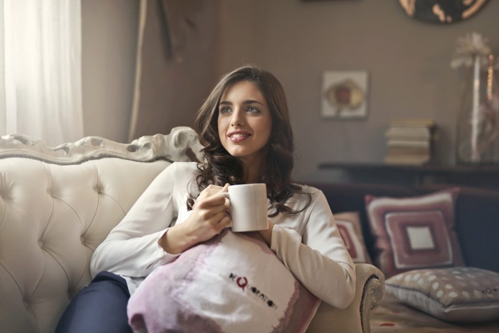 Femme assise sur un canapé, tasse chaude à la main, moment de pause pour apaiser le stress digestif